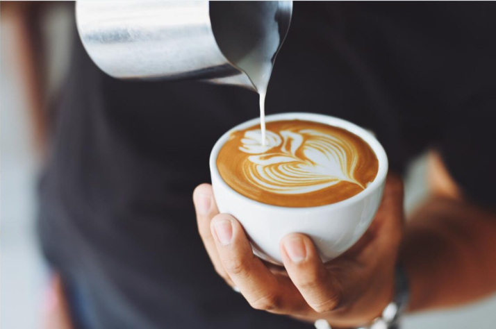 Barista gießt Milch in einen Cappuccino mit Latte-Art